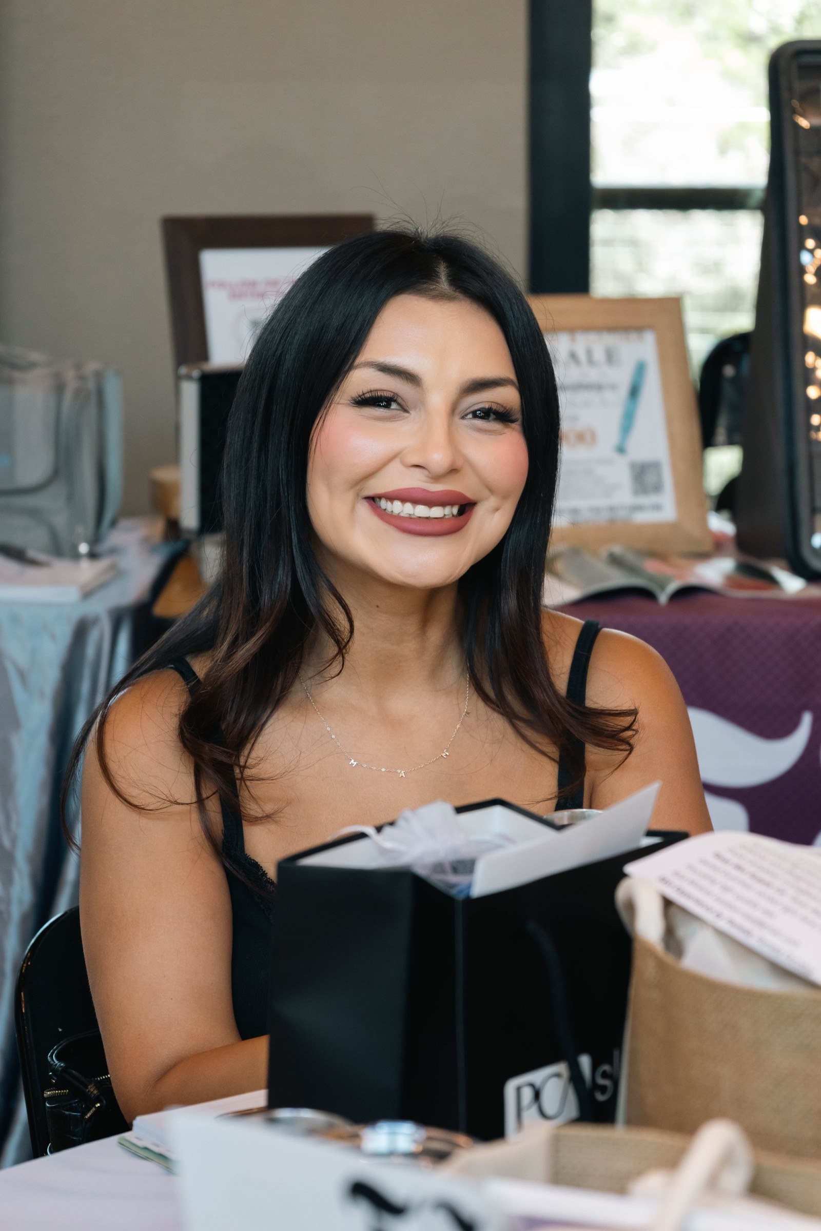 A smiling Glow & Gather attendee seated at a table with event gifts
